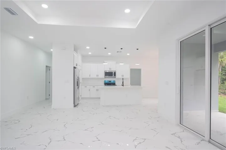 Unfurnished living room with a tray ceiling, recessed lighting, and light marble finish floors