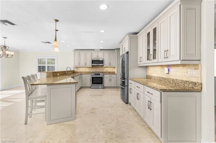 Spacious kitchen featuring a large breakfast bar, stone countertops, light-toned cabinetry, a built-in oven, and a French door refrigerator