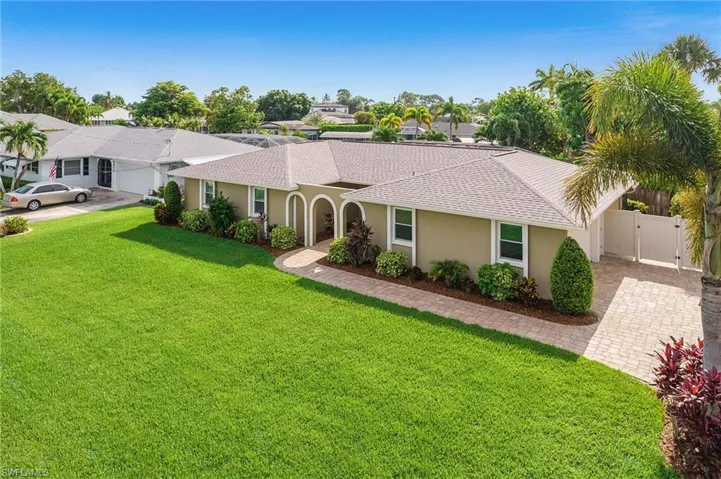 Expansive green lawn fronts a stucco exterior home featuring a curved entry archway and a paver walkway