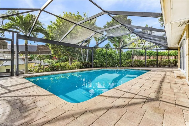 Screened swimming pool enclosure featuring a rectangular pool, paver deck, and lush perimeter landscaping