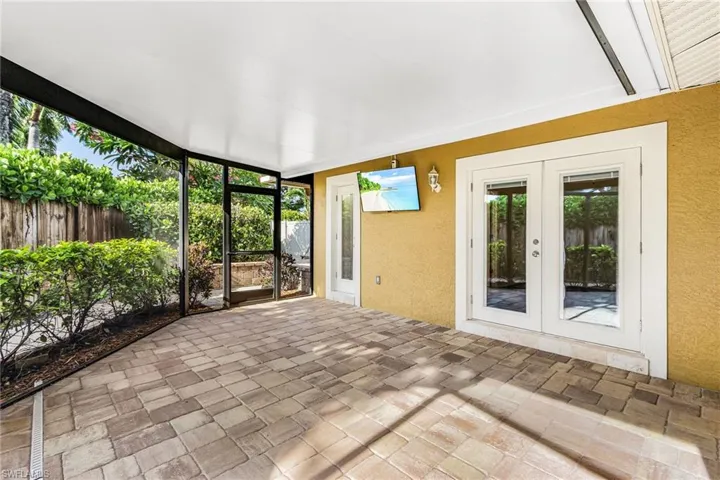 Screened outdoor living area featuring paver flooring, a flat ceiling, and two sets of glass-paned French doors