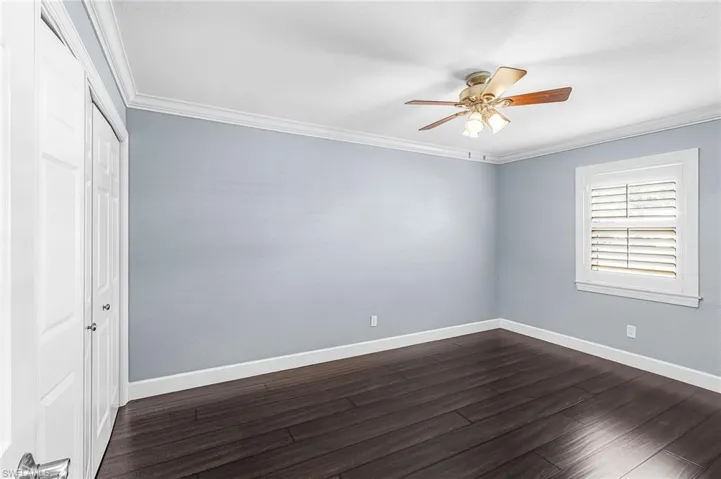 Spacious room featuring dark wood-finish flooring, light blue walls, and white crown molding