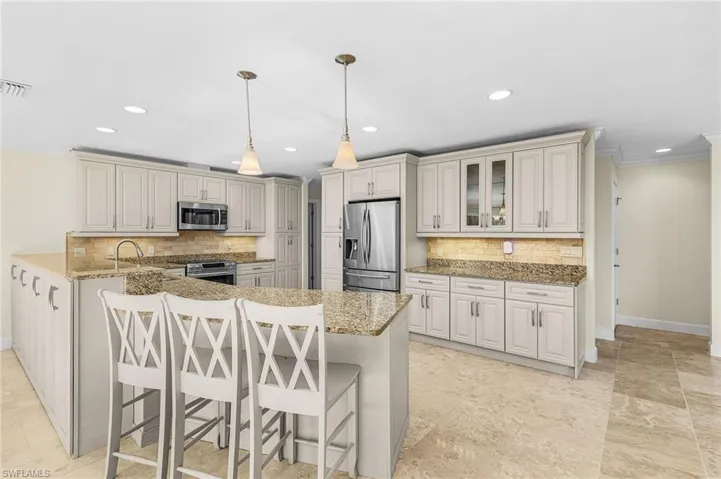 Spacious kitchen featuring an expansive island with pendant lighting, granite countertops, tile backsplash, stainless steel appliances, and extensive cabinetry