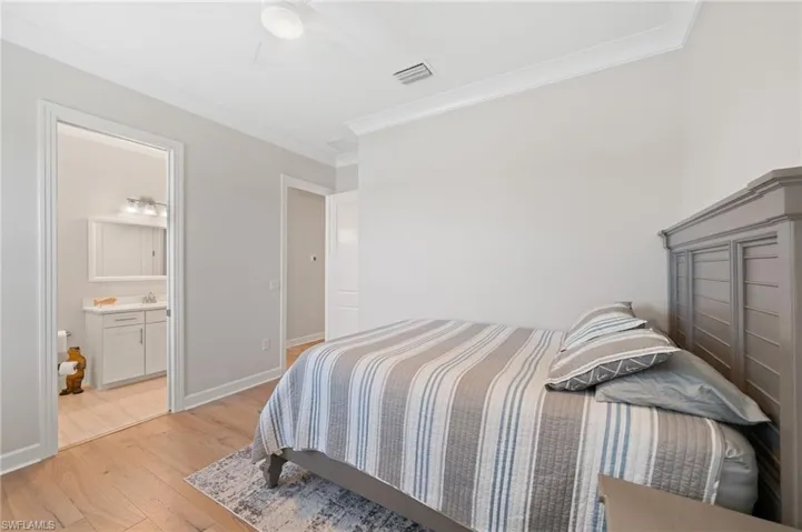 Bedroom featuring light hardwood, crown molding, ensuite bath, and ceiling fan