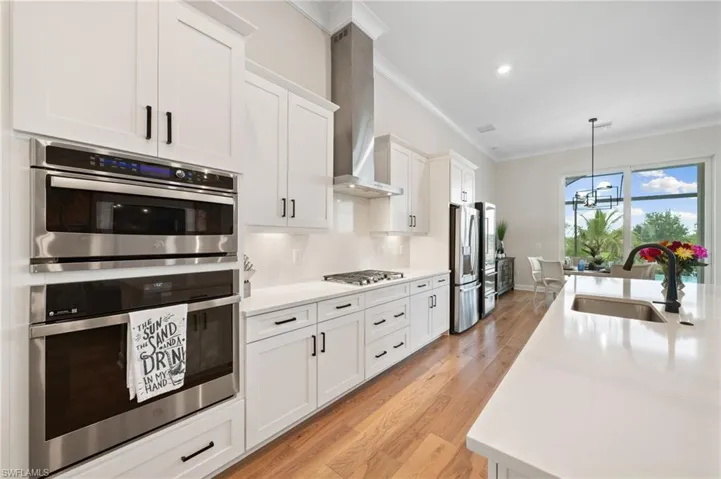 Kitchen with white cabinetry, light wood flooring, wall exhaust hood, sink, and appliances with stainless steel finishes