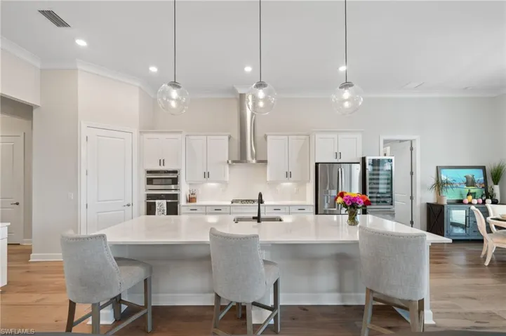 Kitchen featuring hardwood floors, a kitchen island with sink, stainless steel appliances, and wall exhaust hood