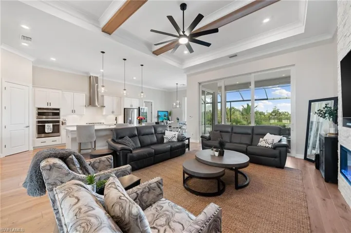 Living room with a tray ceiling, light hardwood floors, crown molding, and ceiling fan