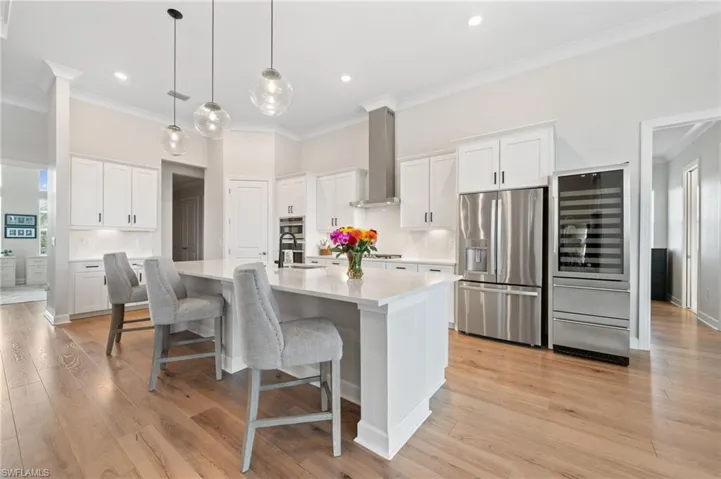 Kitchen with light hardwood floors, appliances with stainless steel finishes, white cabinets, and wall exhaust hood