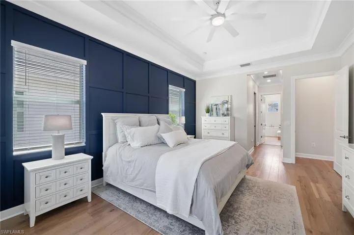 Bedroom with ceiling fan, a tray ceiling, double crown molding, hardwood flooring, and connected bathroom