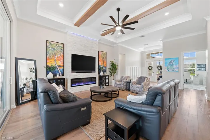 Living room featuring beam ceiling, light wood flooring, ceiling fan, a fireplace, and crown molding