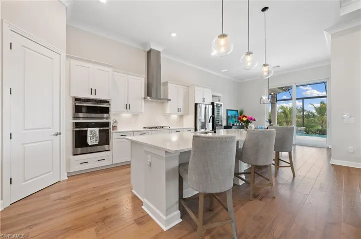 Kitchen with GE Profile stainless steel appliances, a kitchen island with sink, light wood flooring, a kitchen breakfast bar, and wall exhaust hood