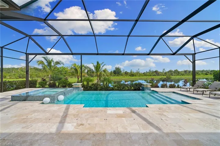 View of infinity edge swimming pool featuring an in ground hot tub, a large lanai, screen enclosure, and a water view