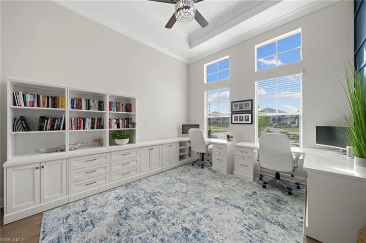 Home office with double crown molding, ceiling fan, light hardwood floors, and a tray ceiling