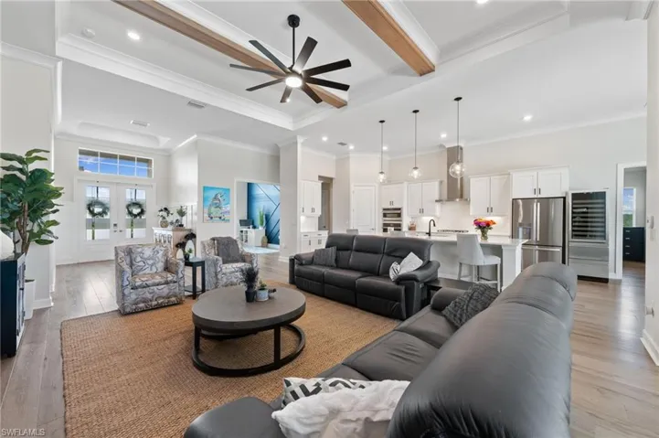 Living room featuring beamed ceiling, light hardwood flooring, ceiling fan, and french doors and crown molding
