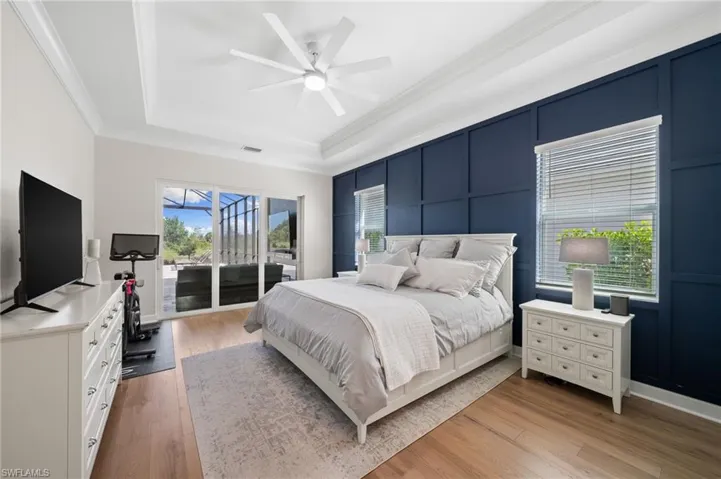 Bedroom featuring light hardwood floors, tray ceiling, double crown molding, multiple windows and sliders