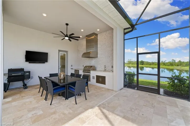 Outdoor kitchen with a beverage fridge, sink, ceiling fan, TV area, dining area and water view