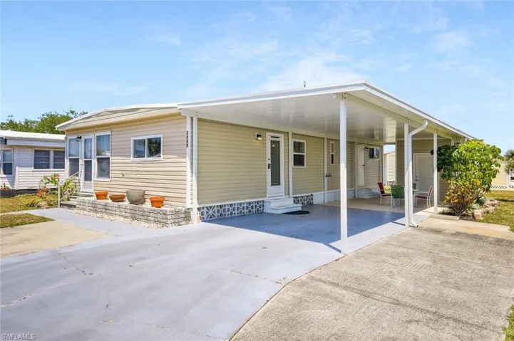 Manufactured / mobile home featuring entry steps, concrete driveway, and an attached carport