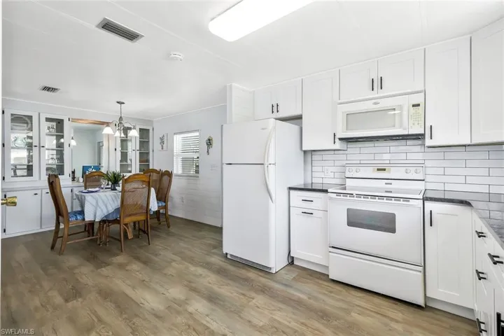Kitchen with dark countertops, light wood-type flooring, visible vents, and white appliances