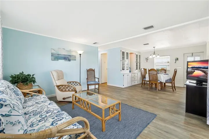 Living area featuring crown molding, visible vents, light wood finished floors, and an inviting chandelier