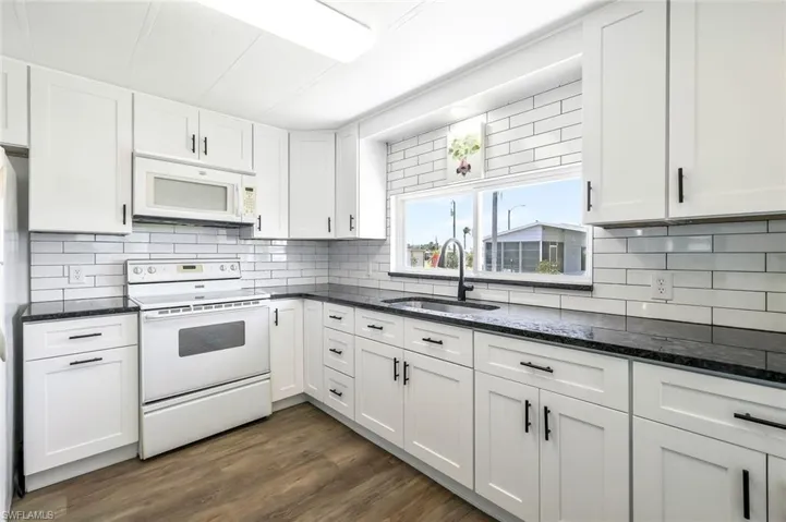 Kitchen featuring tasteful backsplash, dark stone countertops, a sink, white appliances, and white cabinetry