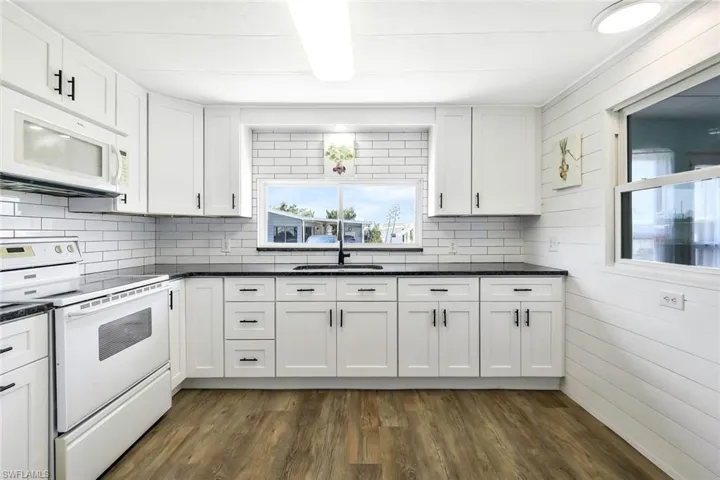 Kitchen with dark countertops, tasteful backsplash, white cabinetry, and white appliances