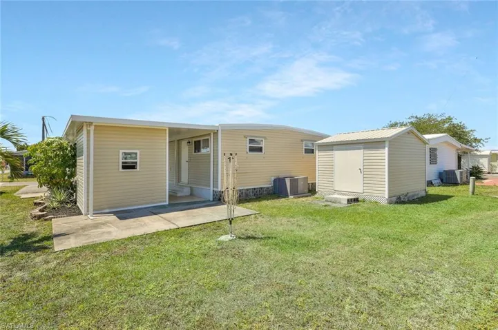 Rear view of house with central AC unit, a yard, an outdoor structure, and a storage unit