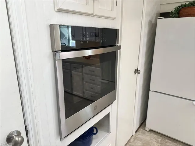 Kitchen with light tile patterned flooring, white fridge, white cabinets, and double oven