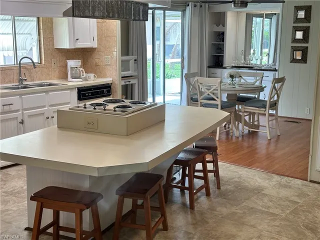 Kitchen with a breakfast bar area, white appliances, white cabinets, a healthy amount of sunlight, and light tile patterned flooring