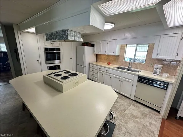 Kitchen with white cabinets, tasteful backsplash, white appliances, and sink