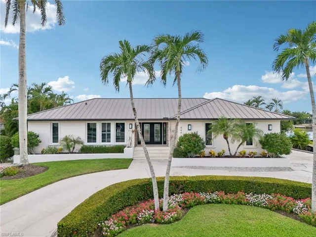 View of front facade featuring stucco siding, curved driveway, a front lawn, and a metal roof