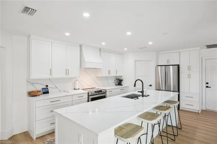 Kitchen featuring light wood-style flooring, a kitchen bar, a kitchen island with sink, custom range hood, and tasteful backsplash