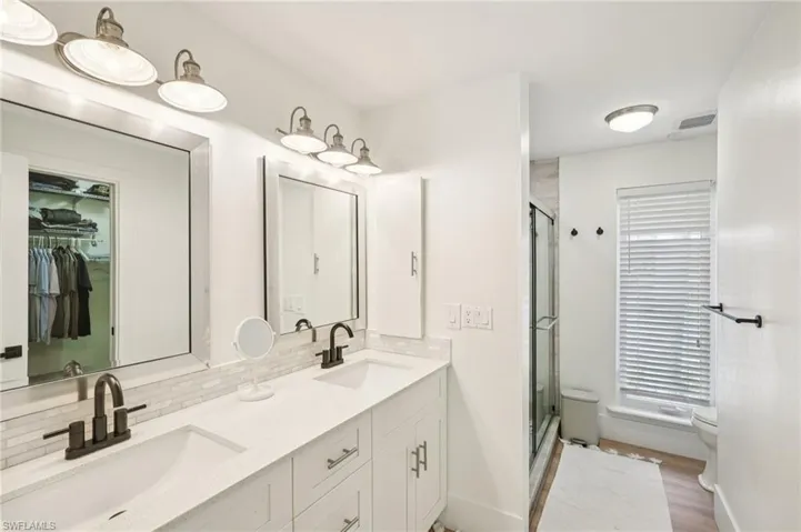Full bathroom featuring tasteful backsplash, a shower stall, double vanity, and a walk in closet