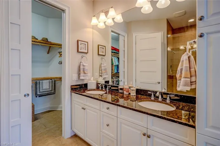 Full bath featuring a spacious closet, light tile patterned floors, double vanity, and a stall shower
