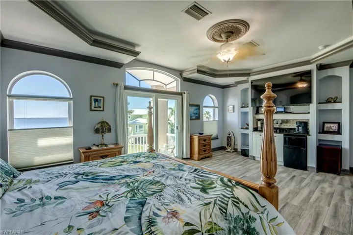 Bedroom with black fridge, ornamental molding, light wood-style flooring, a ceiling fan, and access to exterior