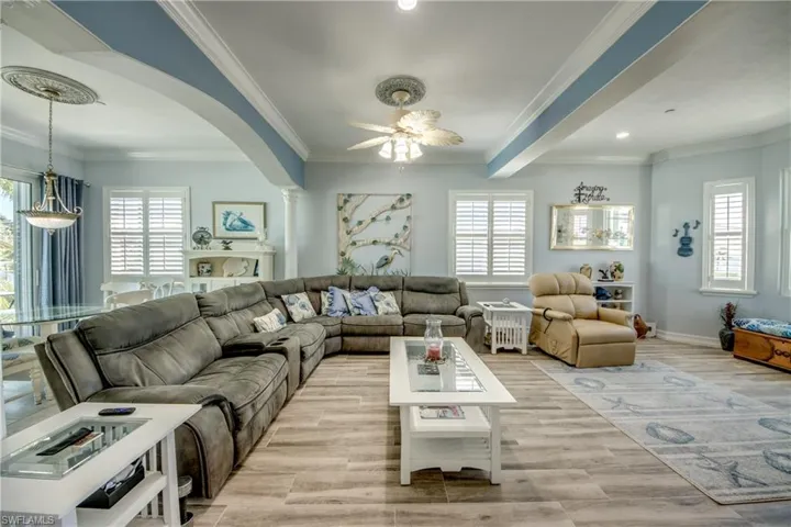 Living room with plenty of natural light, crown molding, light wood-type flooring, arched walkways, and beam ceiling
