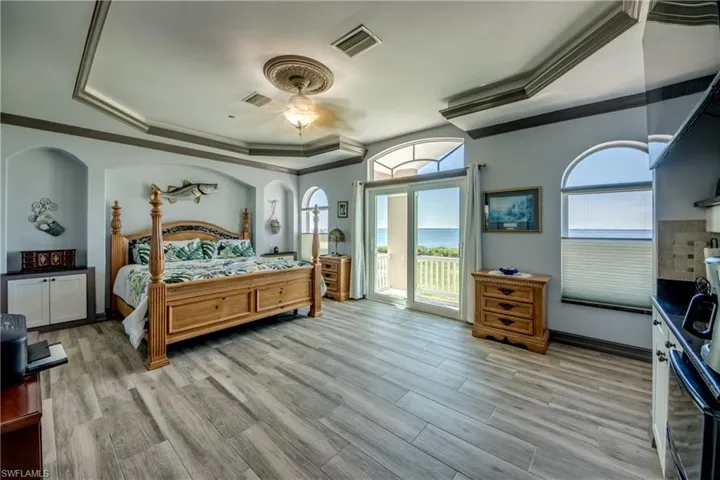 Bedroom featuring ceiling fan, access to exterior, a tray ceiling, and light wood-type flooring