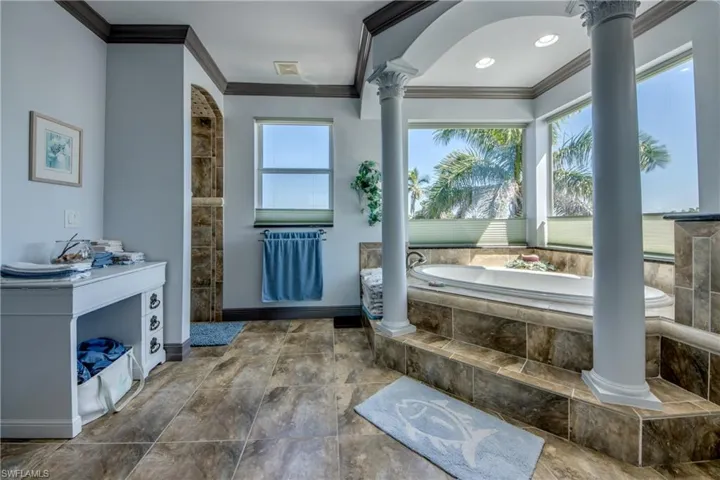 Bathroom with crown molding, a bath, and ornate columns