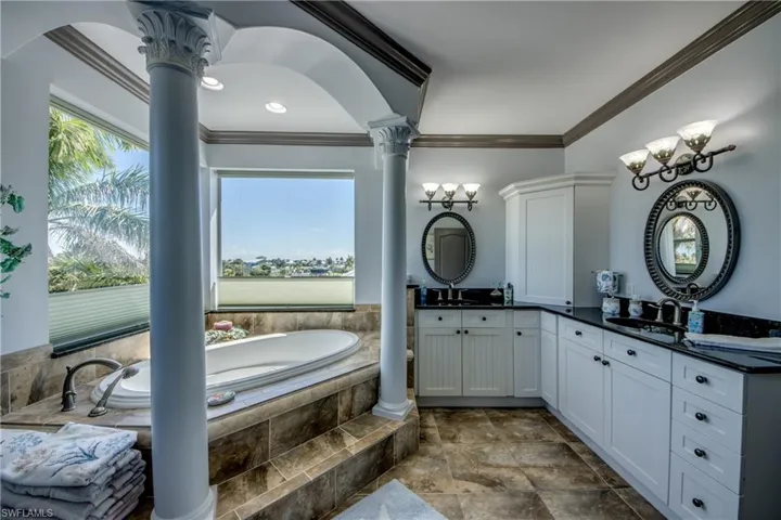 Full bathroom with double vanity, crown molding, a garden tub, and decorative columns
