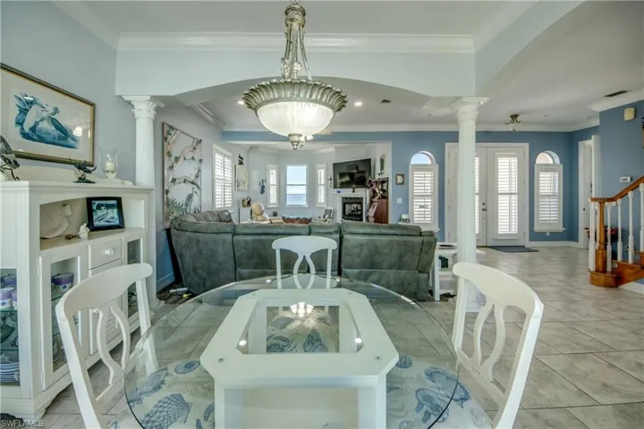 Tiled dining area with ornate columns, crown molding, arched walkways, and stairway