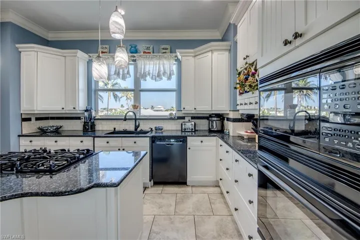 Kitchen featuring dark stone countertops, black appliances, crown molding, white cabinetry, and backsplash