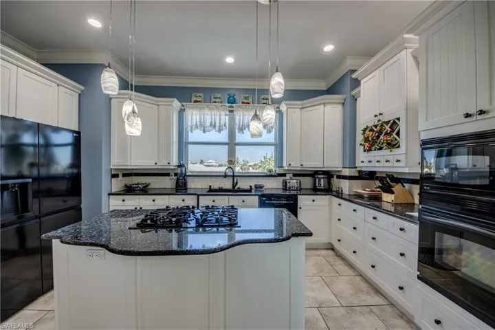 Kitchen featuring black appliances, dark stone countertops, a kitchen island, decorative backsplash, and crown molding