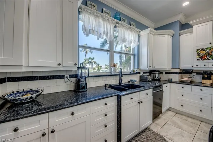 Kitchen with ornamental molding, dark stone counters, decorative backsplash, white cabinetry, and light tile patterned floors