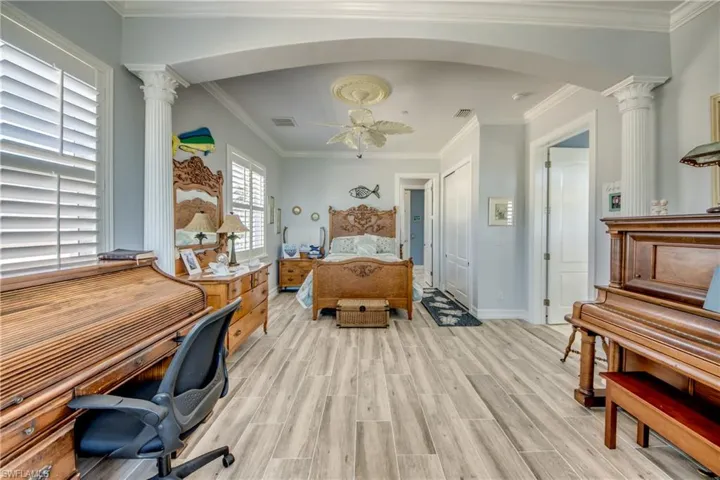 Bedroom featuring arched walkways, crown molding, decorative columns, wood tiled floors, and ceiling fan