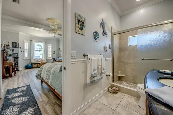 Ensuite bathroom with crown molding, a stall shower, healthy amount of natural light, a wainscoted wall, and ceiling fan