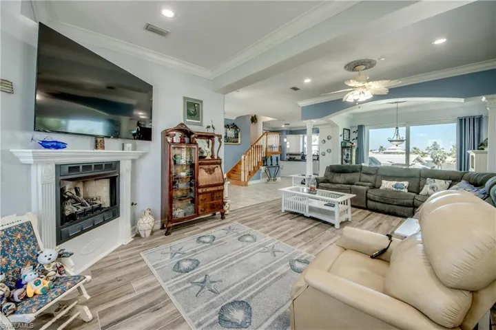 Living room featuring crown molding, a fireplace, wood finished floors, stairway, and ornate columns