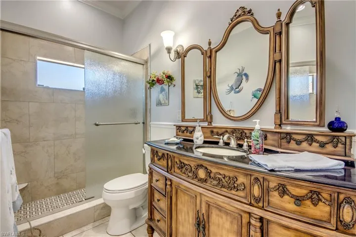 Bathroom with a stall shower, vanity, ornamental molding, wainscoting, and light tile patterned floors