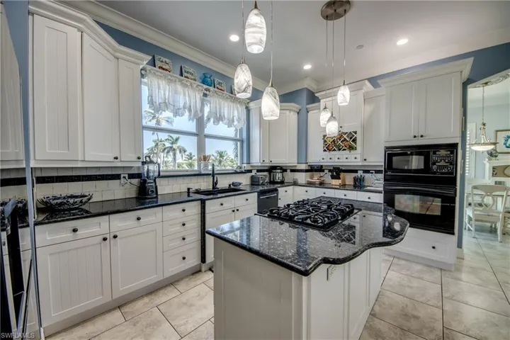 Kitchen with dark stone counters, ornamental molding, a center island, backsplash, and black appliances