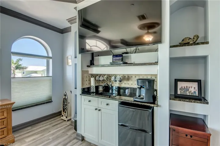 Bar area with fridge, dark stone countertops, open shelves, tasteful backsplash, and light wood-type flooring