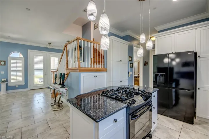 Kitchen featuring crown molding, dark stone countertops, black appliances, and white cabinetry
