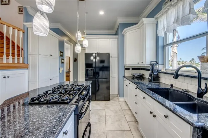 Kitchen featuring dark stone counters, gas range, black fridge, white cabinetry, and ornamental molding